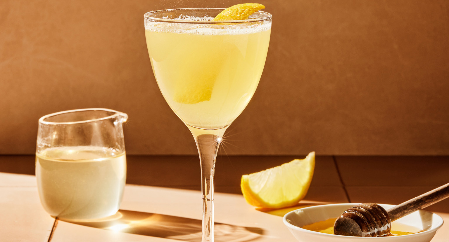 Stettglass med gul drikke og sitron og honning på bordet.