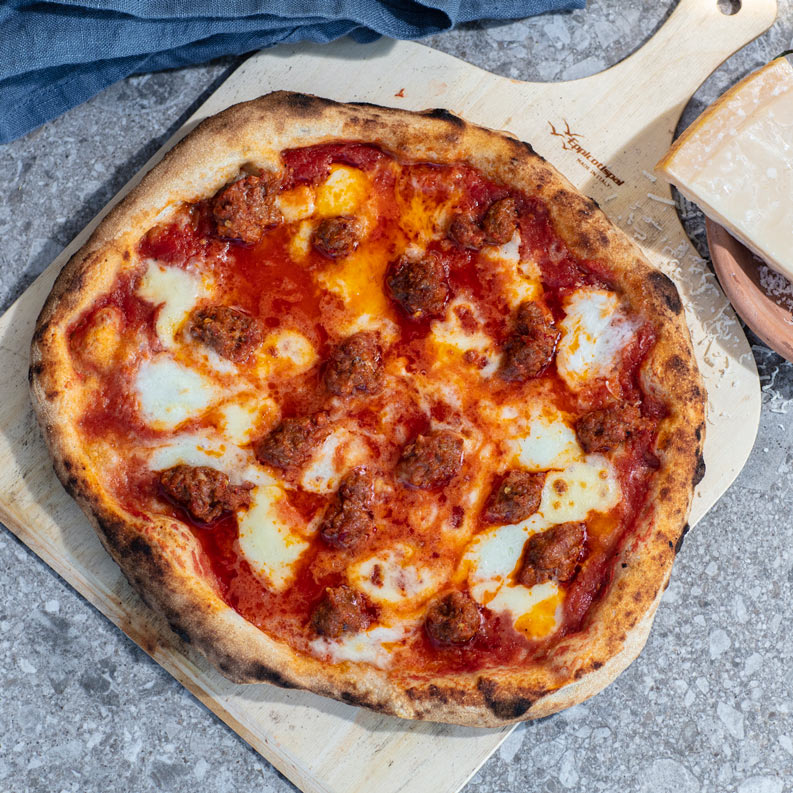 bord med pizzaspade med pizza toppet med tomatsaus, chilipølse og mozzarella
