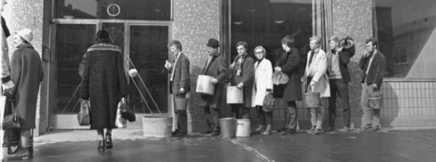 sort-hvitt bilde av folk med bøtter i kø foran et vinmonopol.