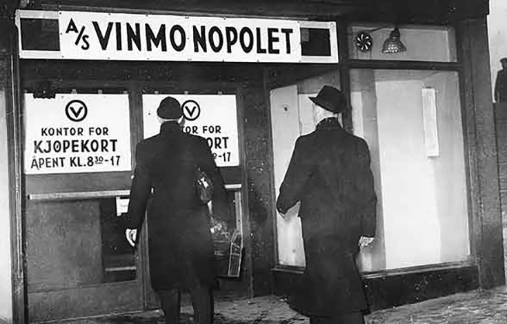 To menn i hatt og frakk går mot en dør med skiltene &quot;A/S Vinmonopolet&quot; og &quot;Kontor for kjøpekort&quot;.