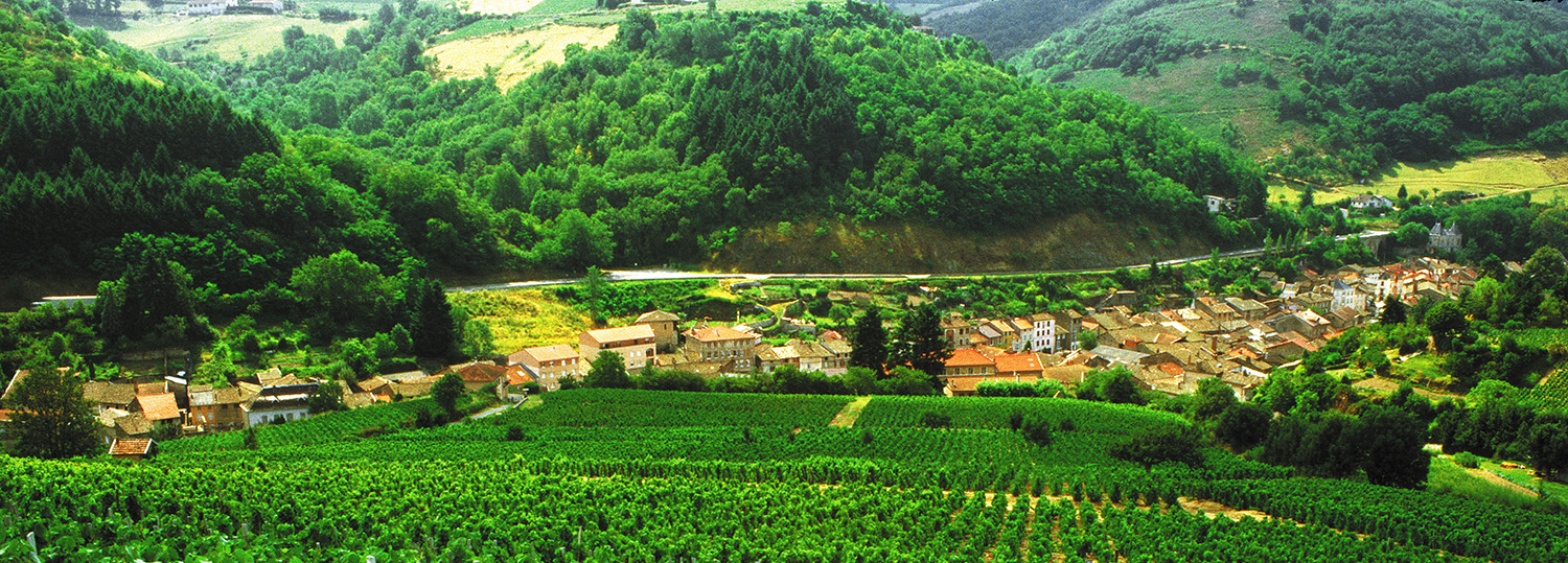 Utsikt nedover et jorde, med landsby i dalbunnen og åssider bakover i bildet.