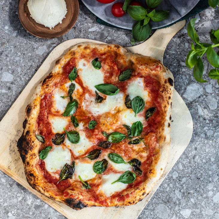 bord med pizzaspade og pizza med tomatsaus, mozzarella og basilikum, fat med tomat, mozzarella og basilikum på siden