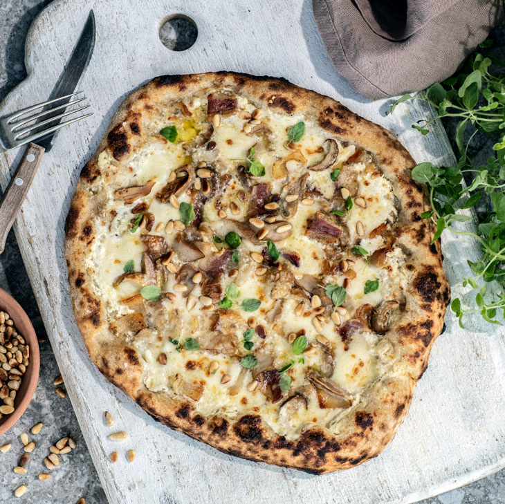 bord med trefjøl og pizza med røkt ost, steinsopp, pinjekjerner og oregano